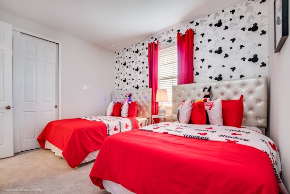 Un dormitorio con dos camas, cada una con ropa de cama roja y almohadas con temática de Mickey Mouse.