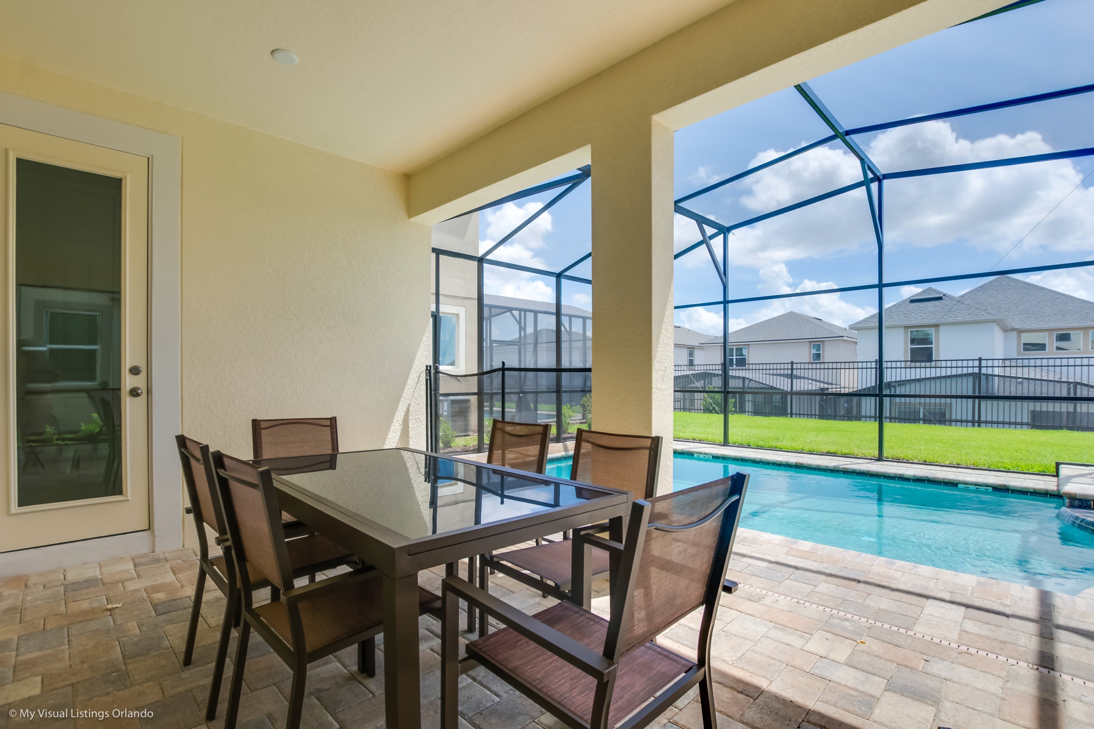 Un patio con una mesa y sillas de vidrio, una piscina y vistas a casas al fondo.