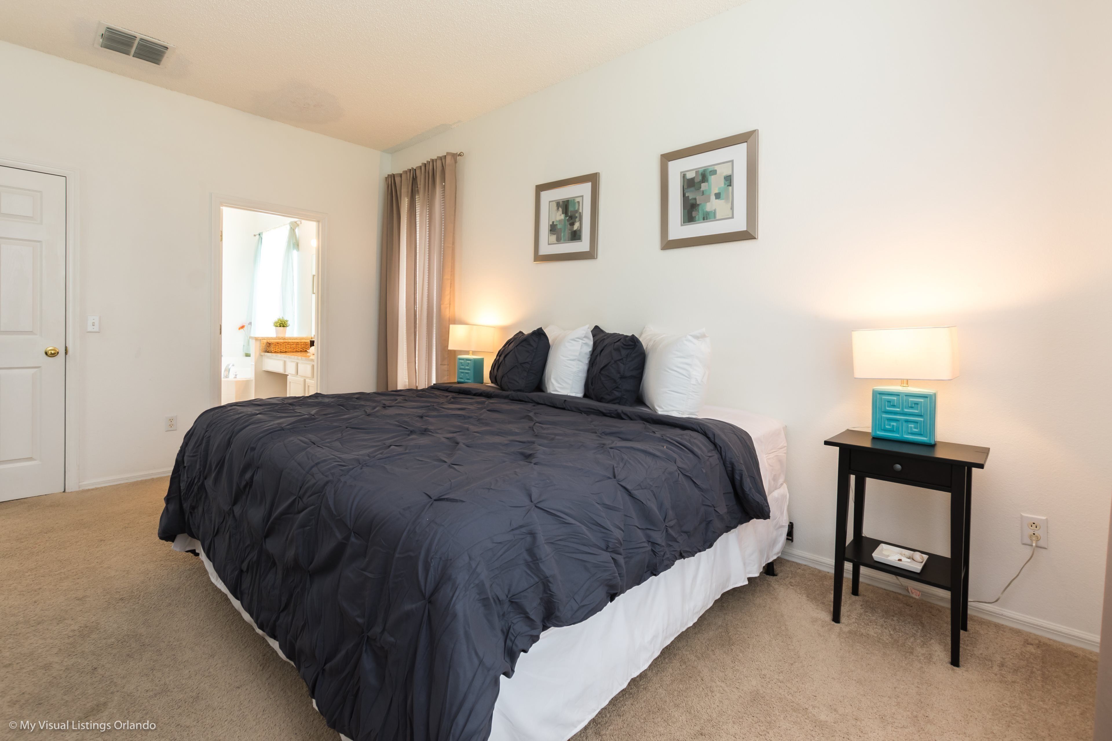A bedroom with a large bed, two bedside tables with lamps, a door, and two framed pictures on the wall.
