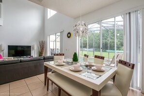 A modern dining area with a glass table set for four, a sofa, and a TV in the background.