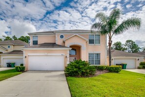 A two-story house with a garage, a well-maintained lawn, and a palm tree.