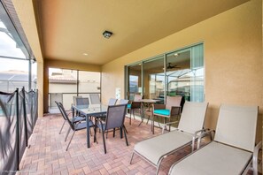 Un patio techado con mobiliario exterior, incluyendo mesas y sillas, y un ventanal que da a un espacio interior.