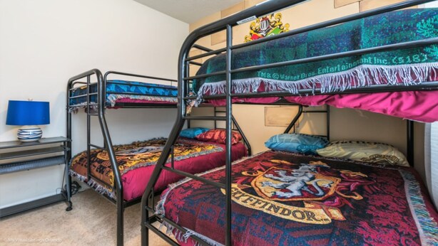 Habitación con literas, una manta con temática de Hogwarts, una mesita con lámpara y un estante en la pared.