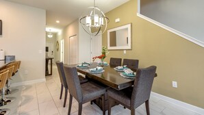 A dining area with a dark wooden table, six gray chairs, and a modern chandelier. - 3084jd000 (Kissimmee)