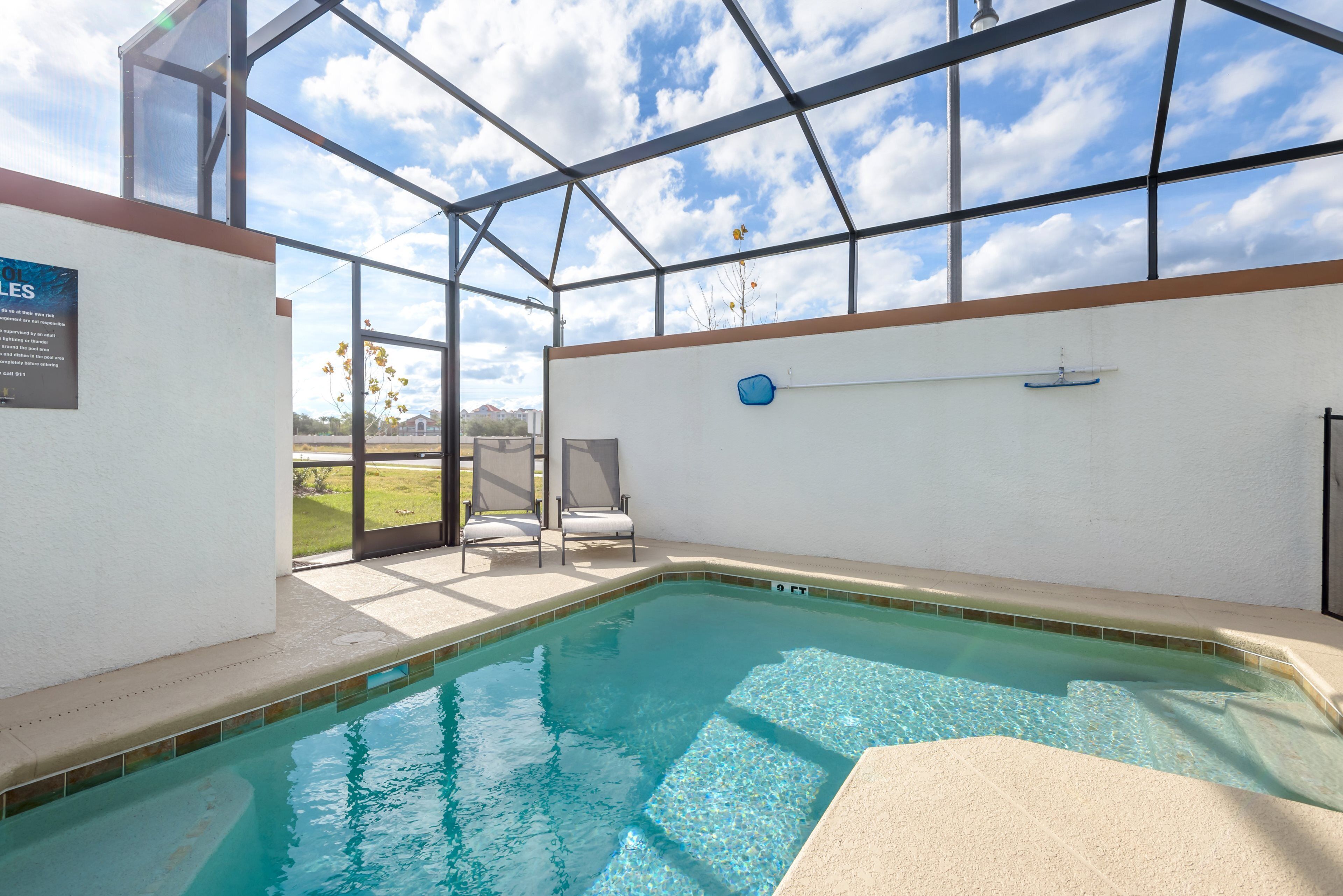 An indoor swimming pool with clear blue water, a glass ceiling, and a view of the outdoors.
