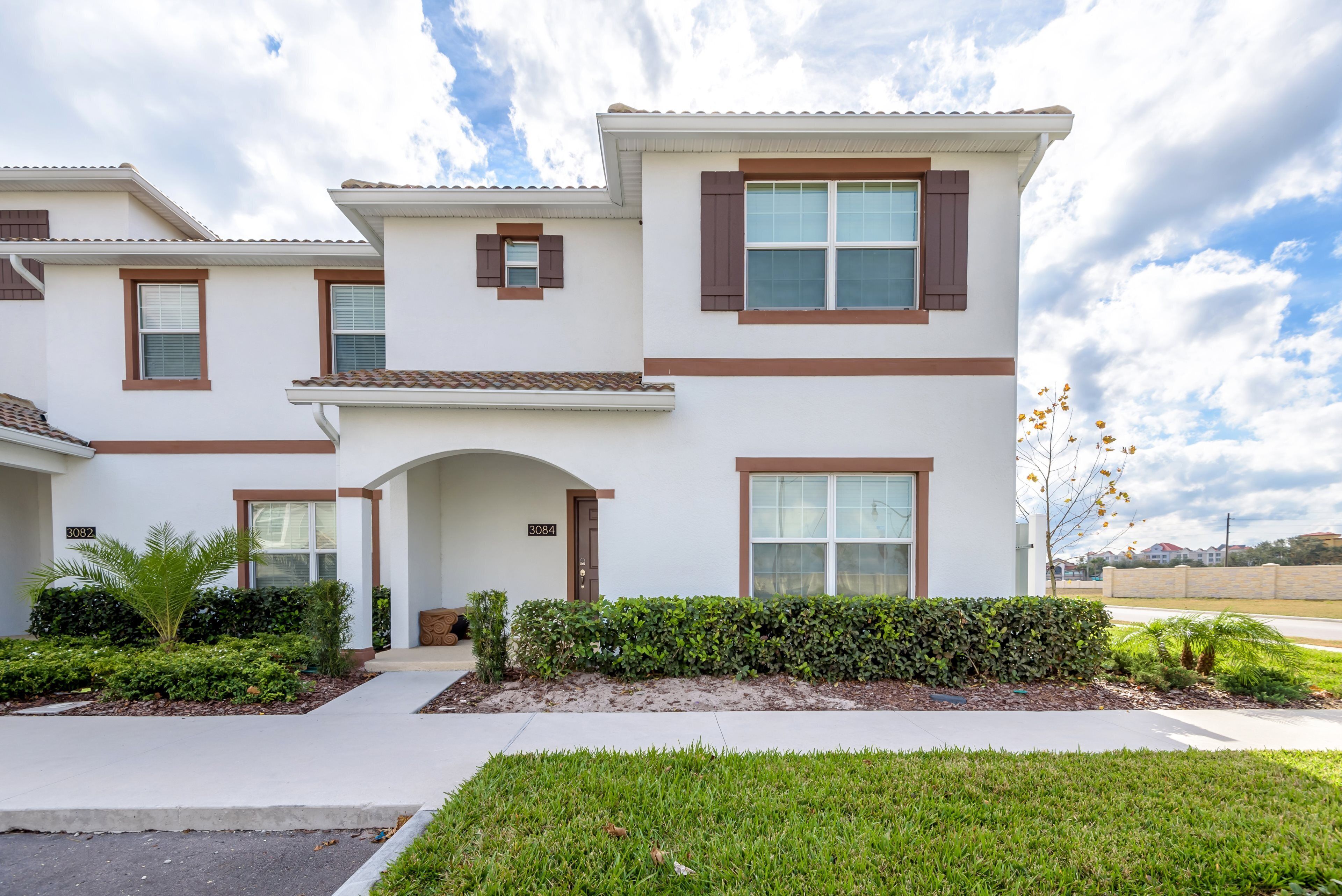 A modern two-story house with a white exterior, brown shutters, and a well-maintained front yard with grass and shrubs.
