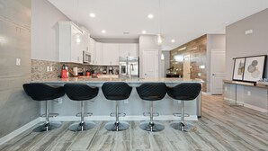 Uma cozinha moderna com ilha central, banquetas, eletrodomésticos de aço inoxidável e iluminação pendente.