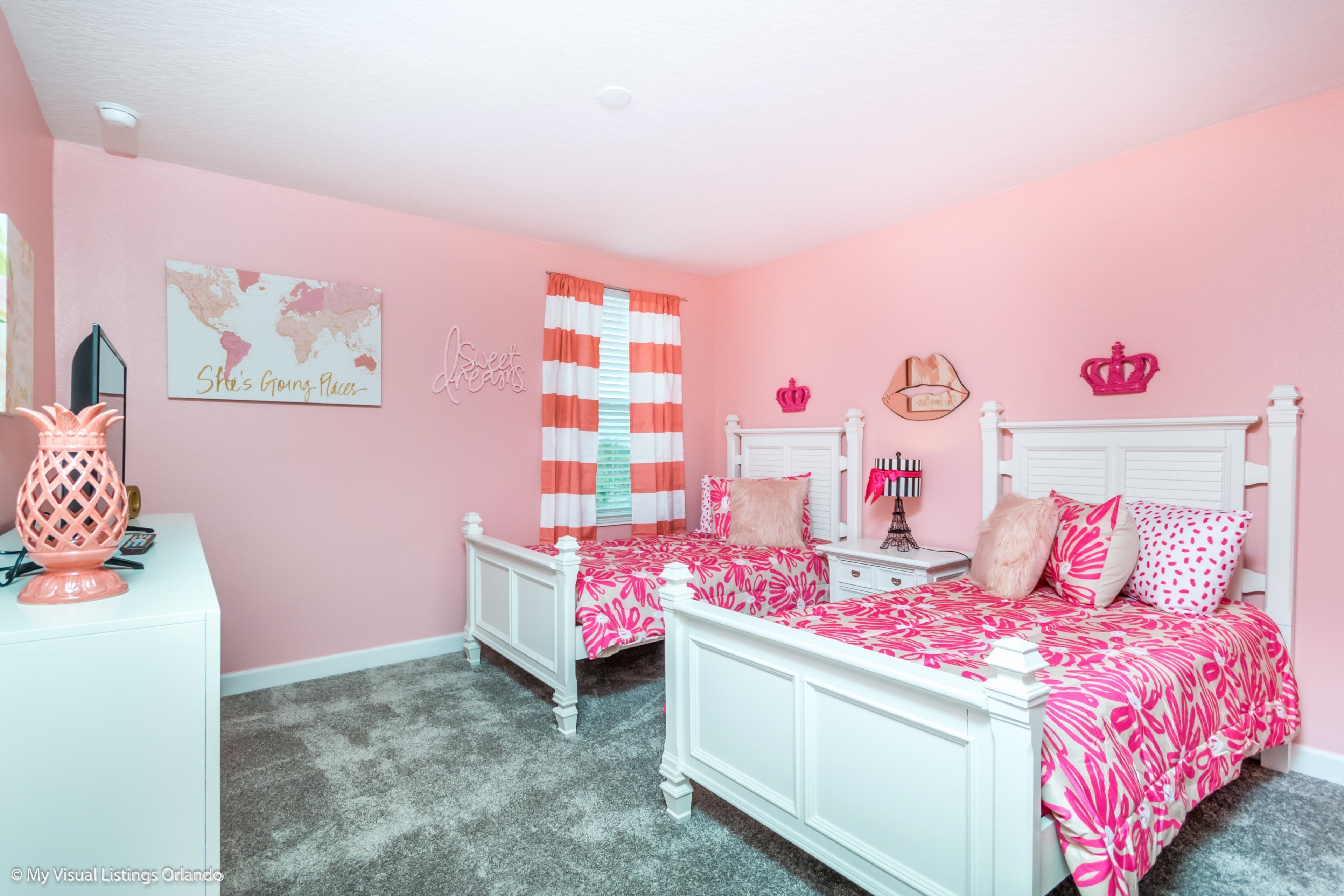 Un dormitorio con decoración rosa, dos camas, un mapa mundial y objetos decorativos.