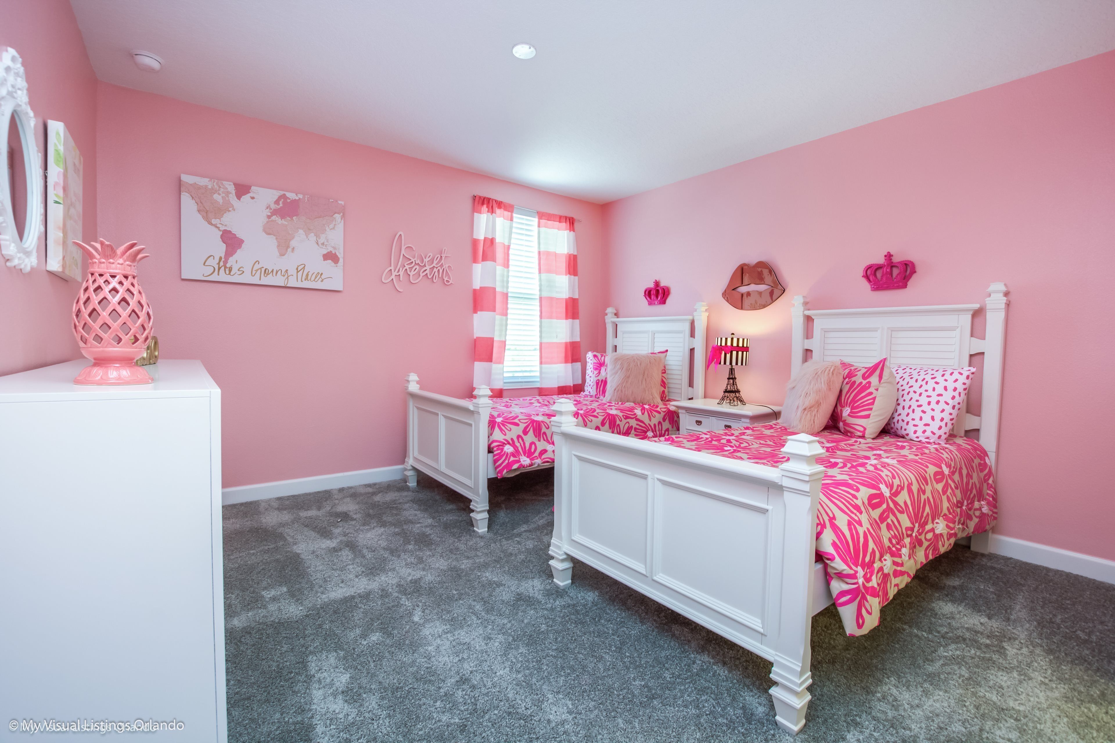 Une chambre à coucher décorée dans des tons de rose, avec deux lits blancs, un globe terrestre et un ananas décoratif.