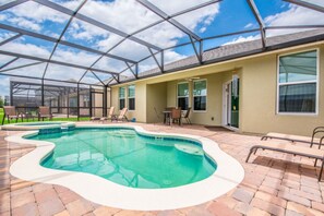 A covered outdoor swimming pool with a brick patio, lounge chairs, and a glass-enclosed structure.