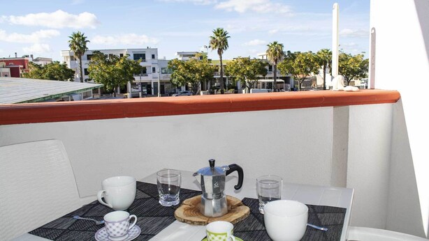 Un balcon avec une table dressée pour deux personnes, comprenant une machine à café, des tasses et des verres.