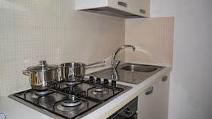 Une cuisine équipée d’une cuisinière à gaz, de casseroles, d’un évier et d’un crédence carrelée de couleur blanche.