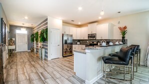 A spacious kitchen with white cabinets, a central island with bar stools, a refrigerator, and a microwave. - 1314bw00 (Davenport)