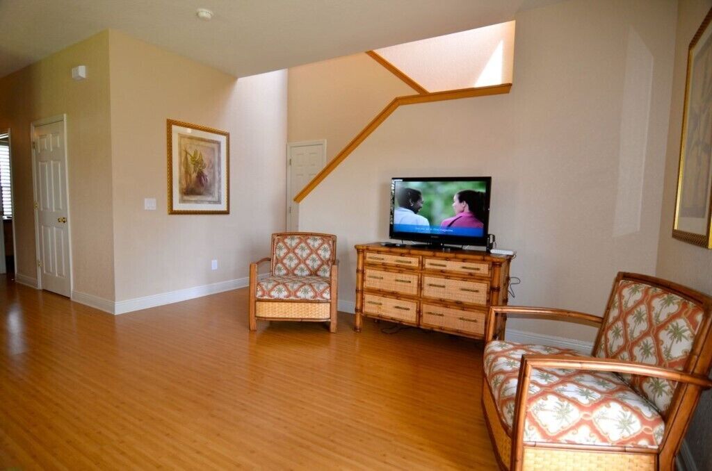 A living room with hardwood flooring, a television, wicker furniture, and a staircase.