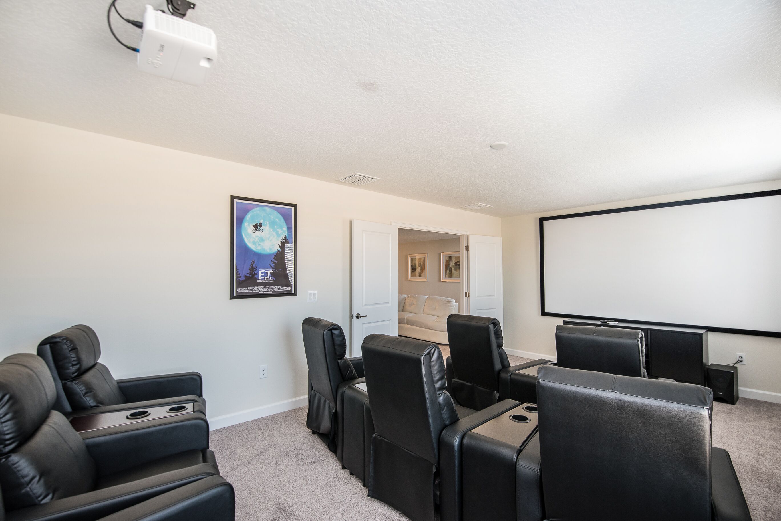 Una sala de cine en casa con sillones reclinables de cuero negro, una pantalla grande y un proyector.