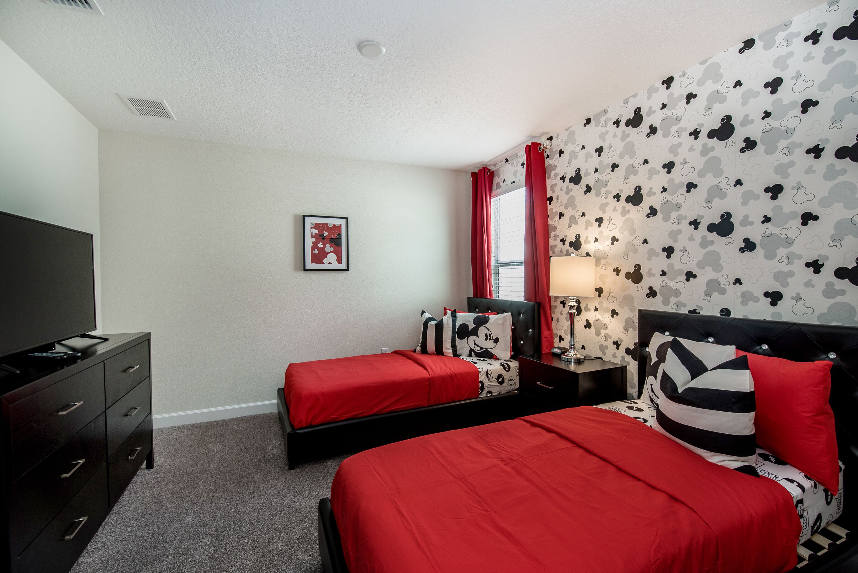 A hotel room with two beds, a TV, a dresser, and a wall with a Mickey Mouse pattern.