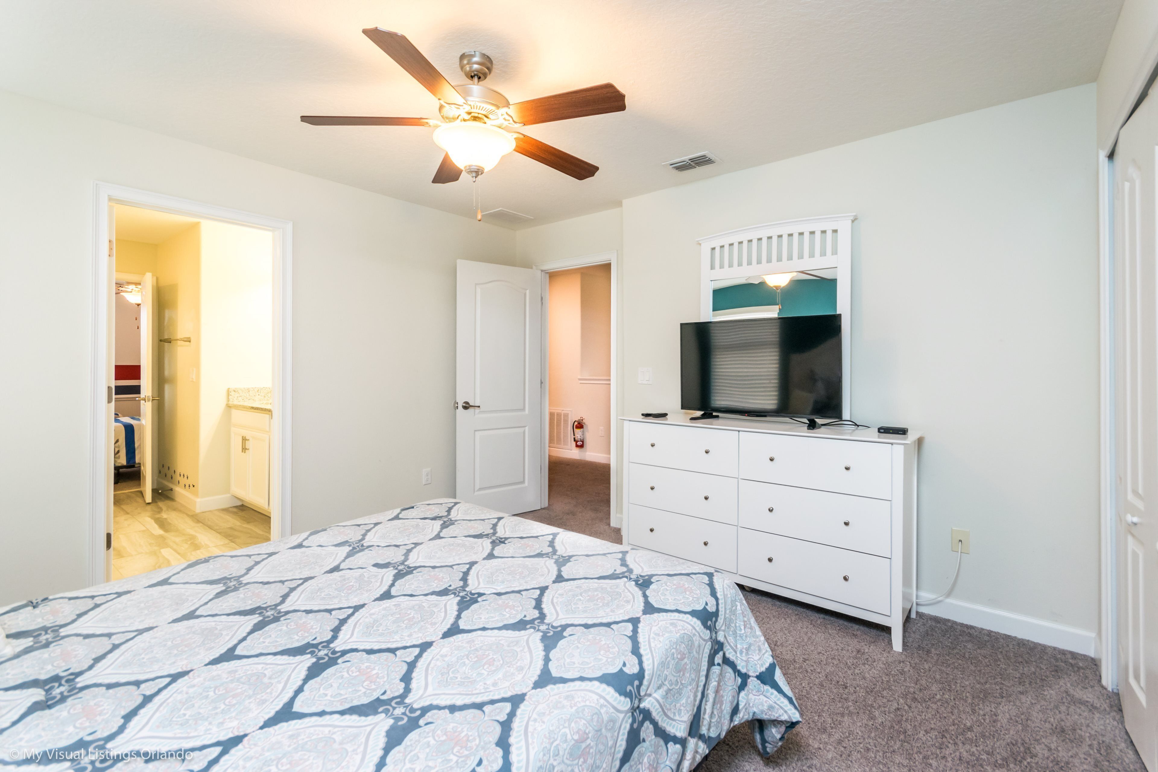 A bedroom with a bed, a dresser, a ceiling fan, and a television.
