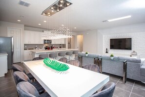 A modern kitchen with white cabinets, a central island, and a dining area with a glass table and chairs. - Luxury Solara 7 Bed Private Pool IHR 1039 (Kissimmee)