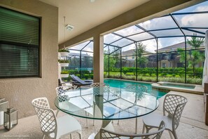 A glass-enclosed outdoor patio with a pool, white chairs, and a round glass table.