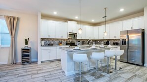 Una cocina moderna con armarios blancos, electrodomésticos de acero inoxidable y una isla central con taburetes de bar.