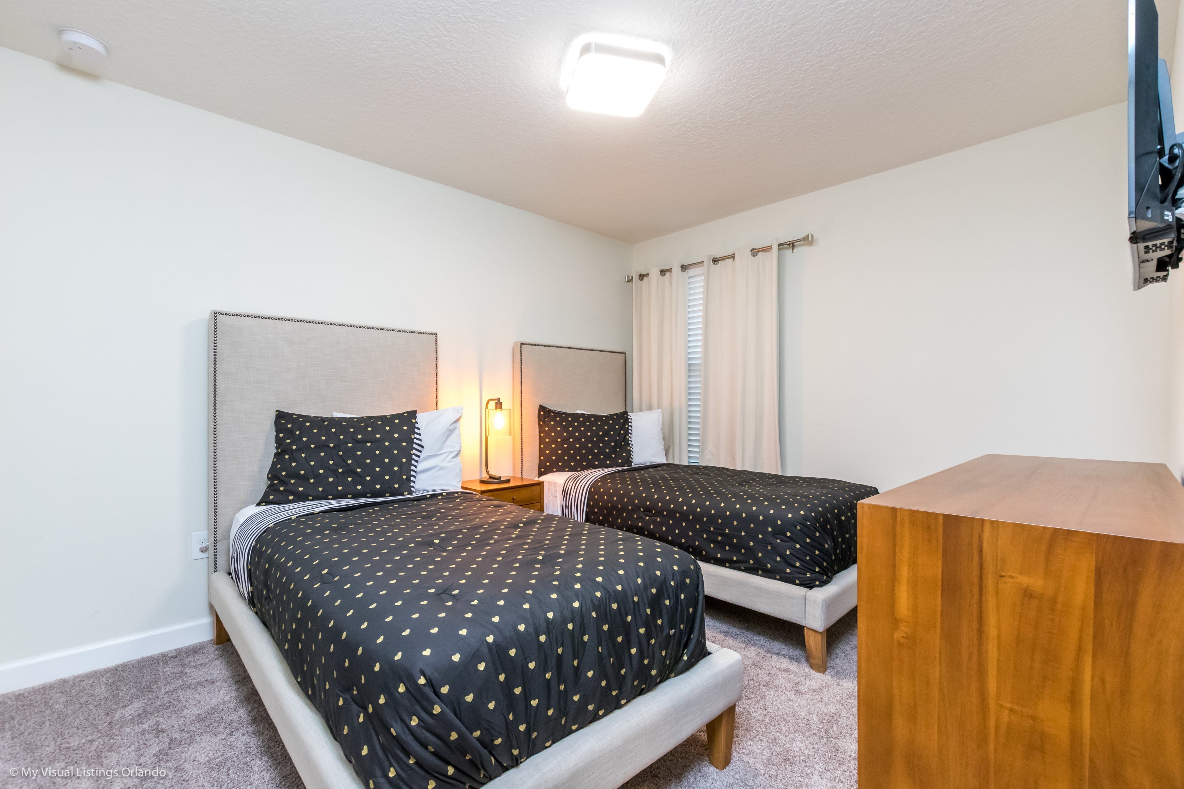 A bedroom with two beds, a bedside table, a lamp, and a wooden nightstand.