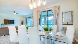 Un comedor moderno con una mesa de vidrio, sillas blancas y un ventilador de techo.