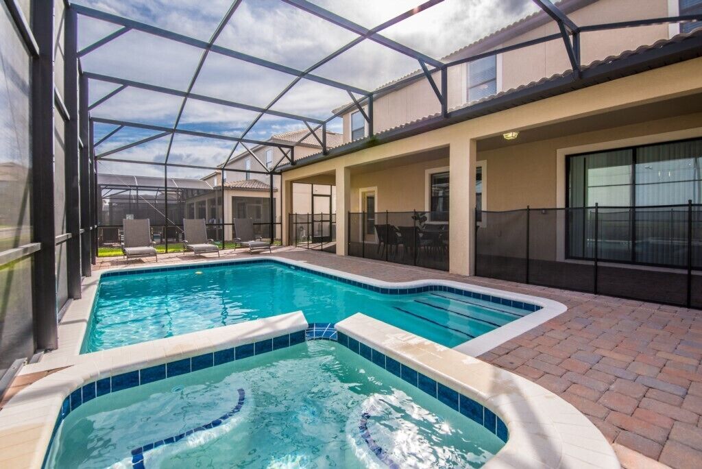 A swimming pool with a glass enclosure, lounge chairs, and a hot tub.