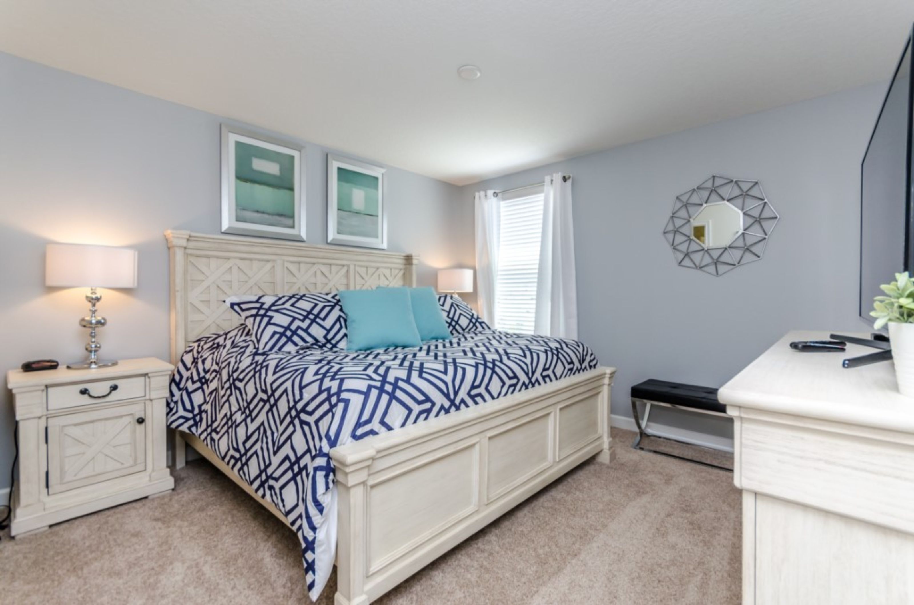 A bedroom with a bed, nightstands, a desk, a mirror, and a window with curtains.