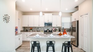 A modern kitchen with white cabinets, a granite countertop, a stainless steel refrigerator, and a central island with bar stools. - 5 Bedroom 5 Bathroom Villa (Davenport)
