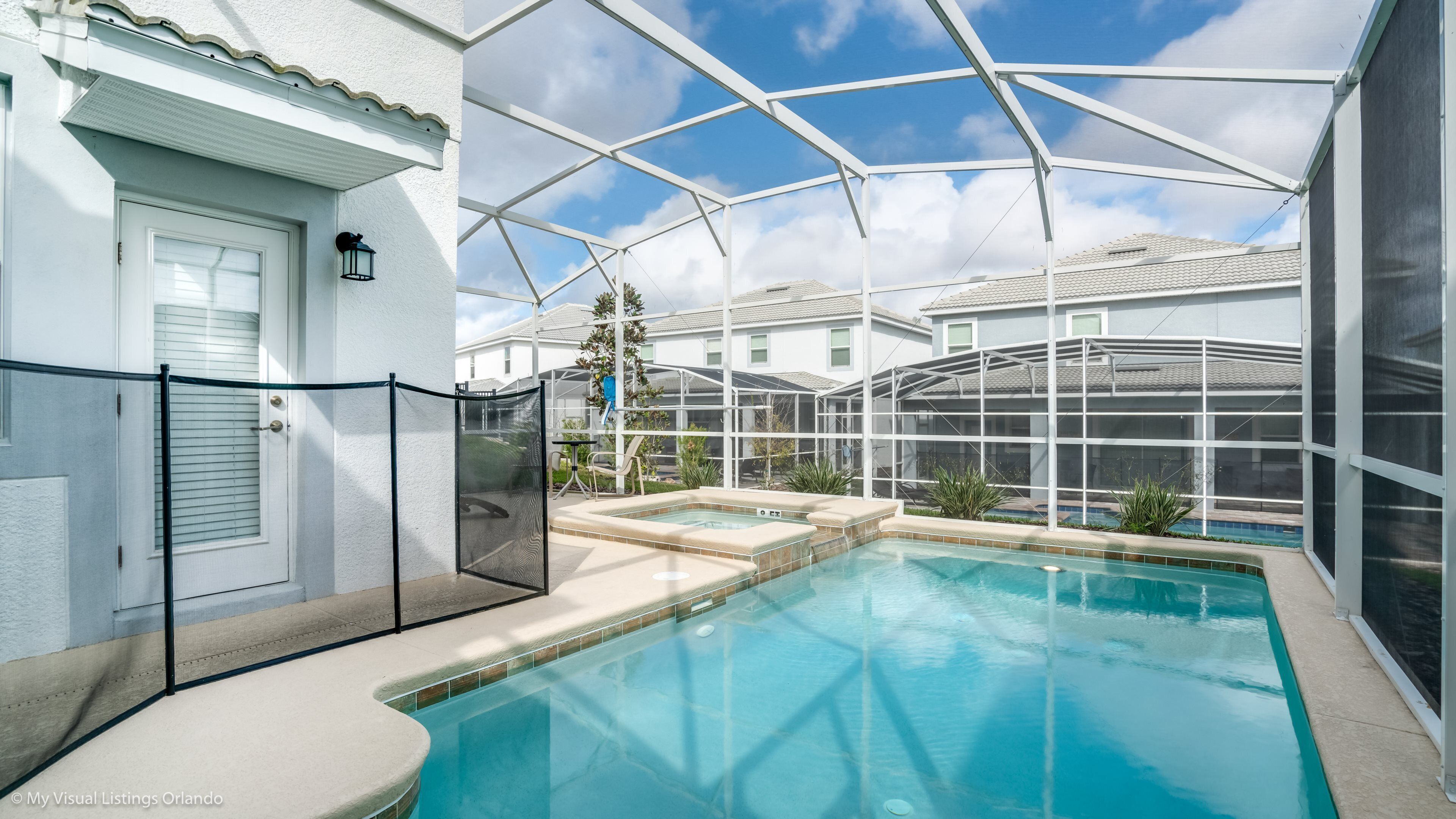 Ein Pool mit Glasveranda, eine überdachte Terrasse und Blick auf umliegende Häuser.