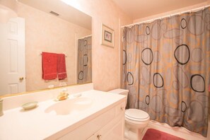 Une salle de bain avec un meuble-lavabo blanc, des toilettes et un rideau de douche à motifs géométriques.