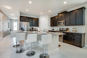 A modern kitchen with dark cabinets, stainless steel appliances, and a central island with bar stools. - 7 Bed 5 Ba Villa with Games, Pool & Spa (Kissimmee)