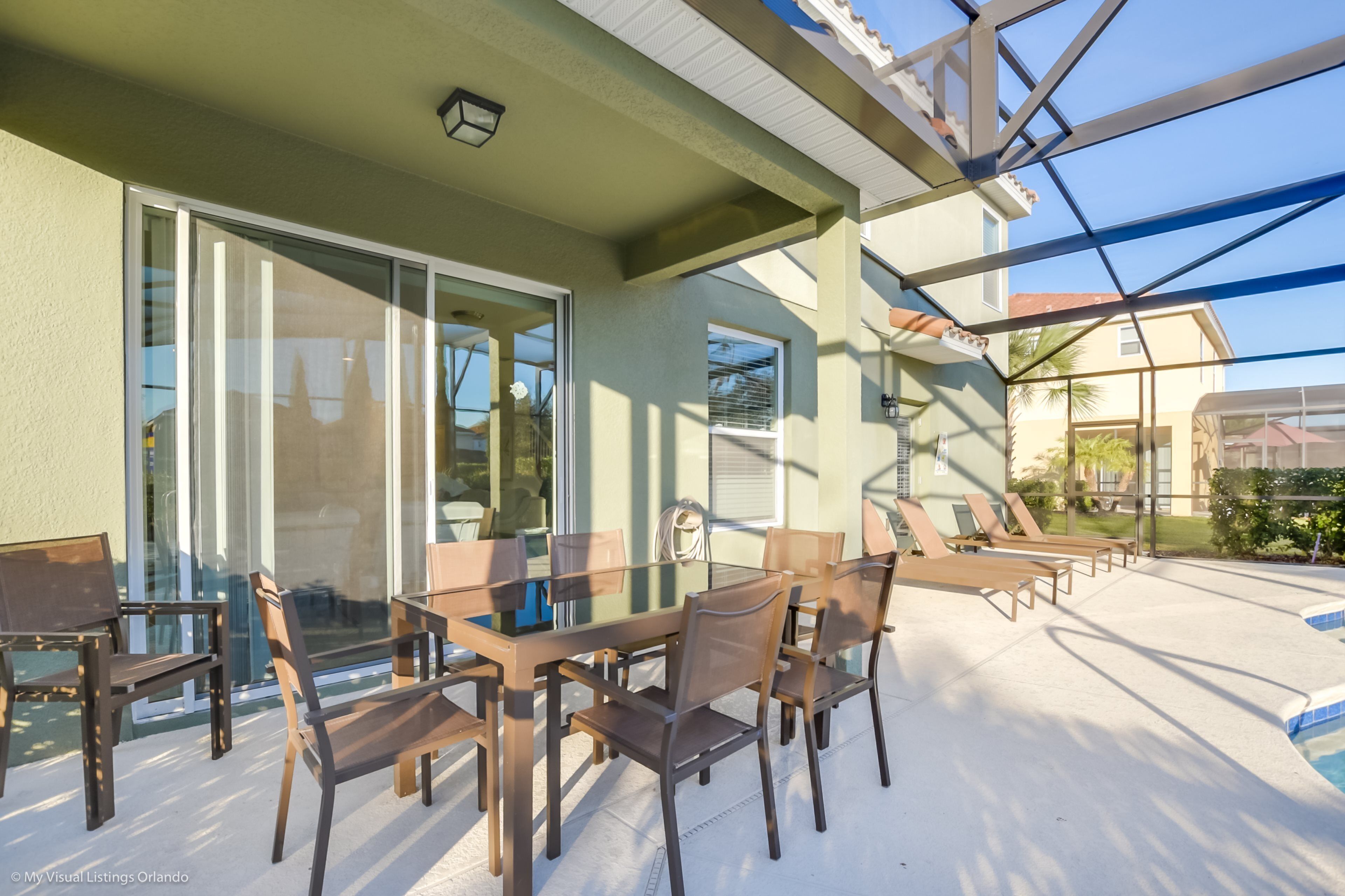 A glass-enclosed patio with a dining table and chairs, a pool, and a covered area with lounge chairs.