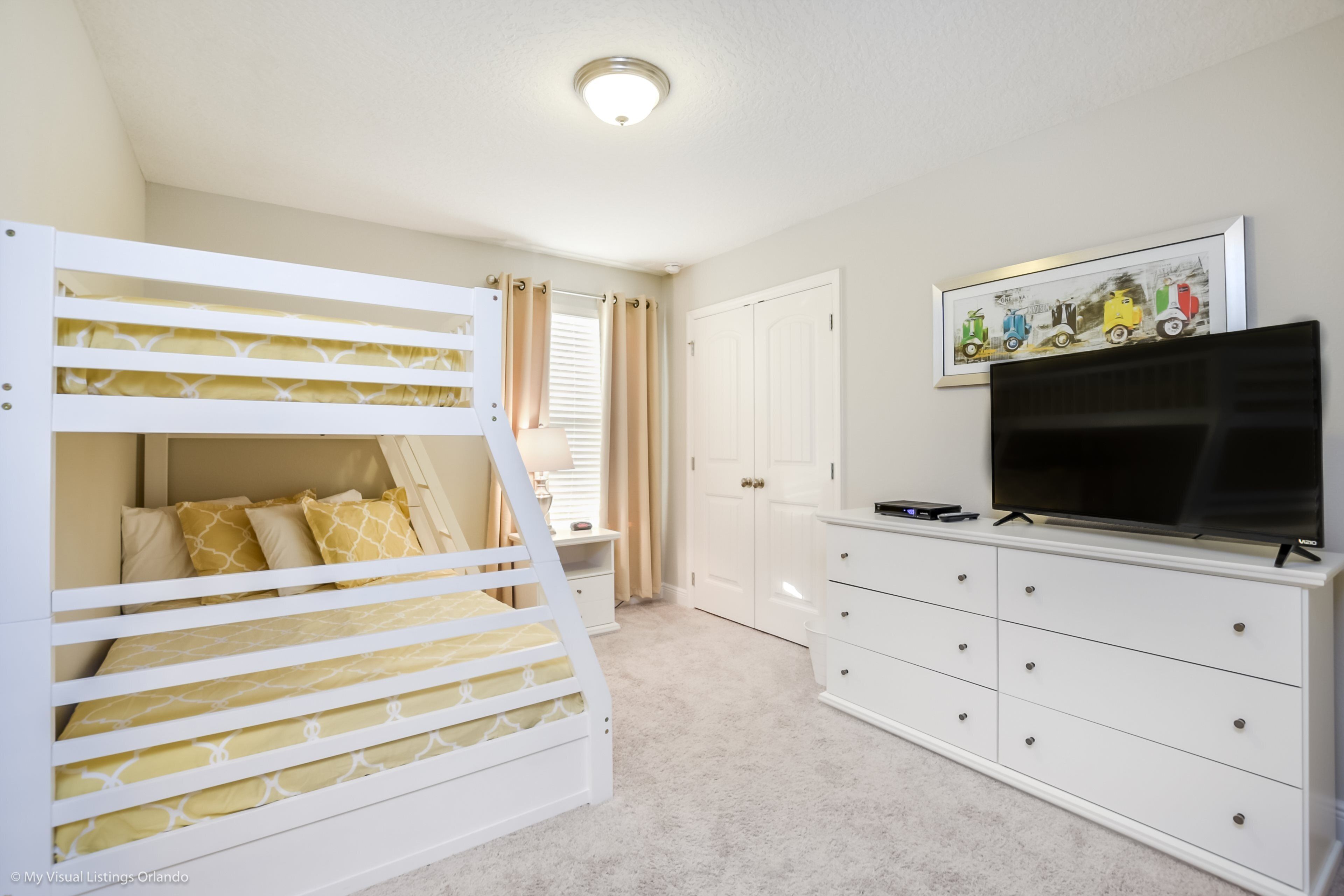 Quarto com beliches, cômoda, televisão e quadro na parede.