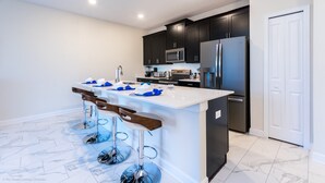 A modern kitchen with dark cabinets, a white island with bar stools, stainless steel appliances, and a white door.