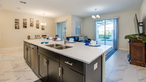 A modern kitchen with a large island, dark cabinetry, and a view to the outside.