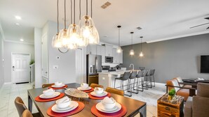 A modern kitchen with stainless steel appliances, a dining area with a wooden table set for four, and a living area with a sofa and coffee table. - Storey Lake Resort 4 Bedroom House (Kissimmee)