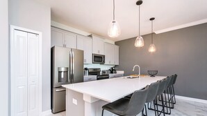 A modern kitchen with white cabinets, stainless steel appliances, and a central island with bar stools. - Storey Lake Resort 4 Bedroom House (Kissimmee)