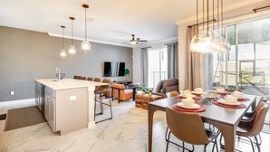 A modern kitchen with a central island, dining area with a long table, and a view of the outdoors through large windows. - Storey Lake Resort 4 Bedroom House (Kissimmee)