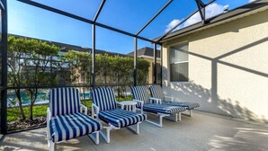 Ein überdachter Außenbereich mit vier gestreiften Liegestühlen und einem kleinen Tisch, mit Blick auf einen Pool und viel Grün.