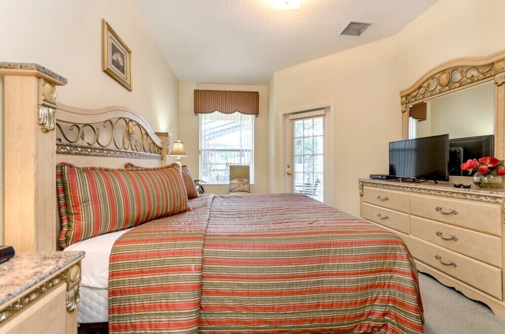 A bedroom with a large bed, a dresser, a television, and a window with curtains.