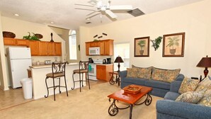 A living room with a blue sofa, a coffee table, and a kitchen area with wooden cabinets and a microwave. - 1915msd (Clermont)
