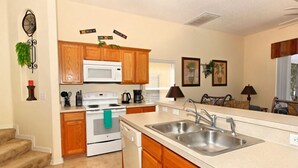 A kitchen with wooden cabinets, a white stove, a microwave, and a double sink. - 1915msd (Clermont)