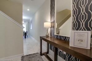 A hallway with a wooden console table, a wall-mounted mirror, and a framed welcome sign.