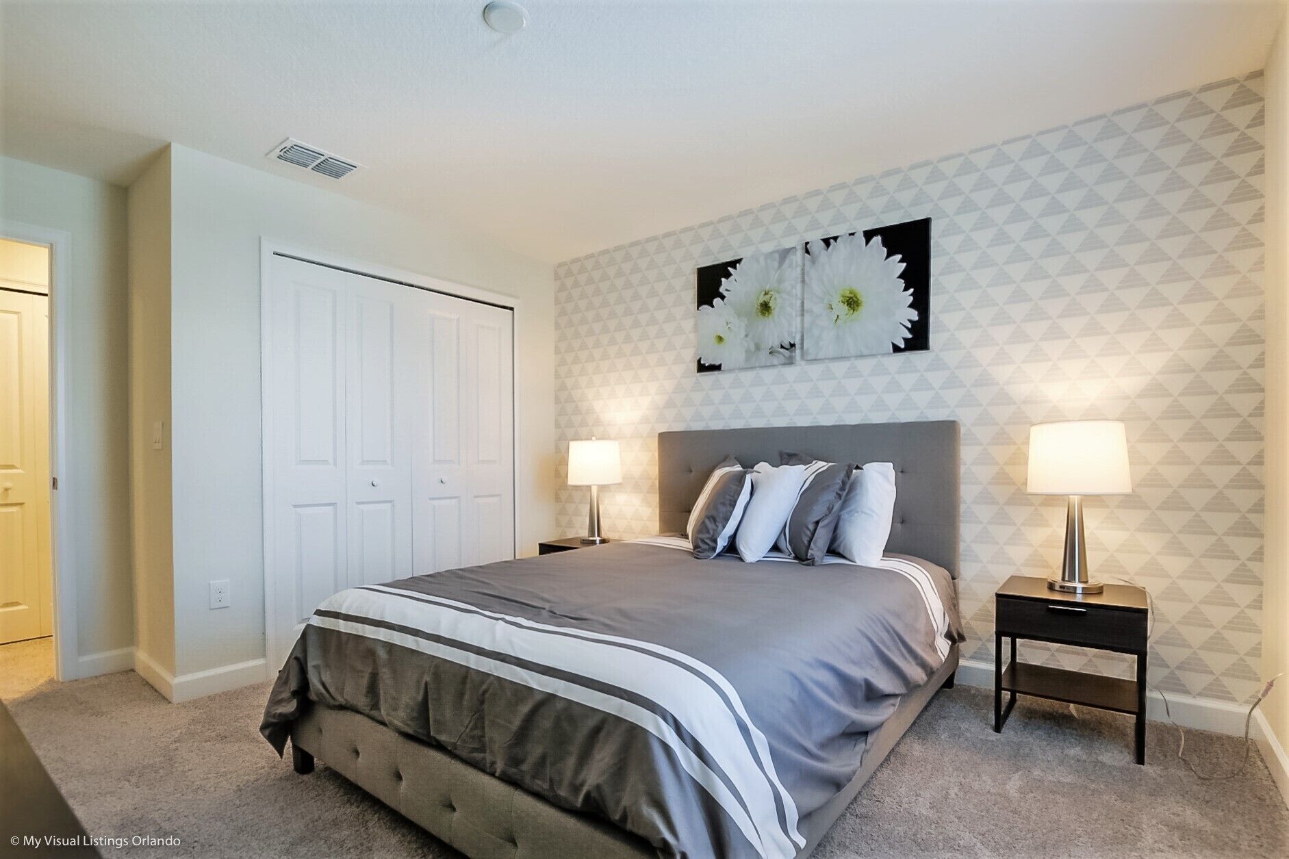 A bedroom with a large bed, two bedside tables, a white door, and a wall with a geometric pattern.