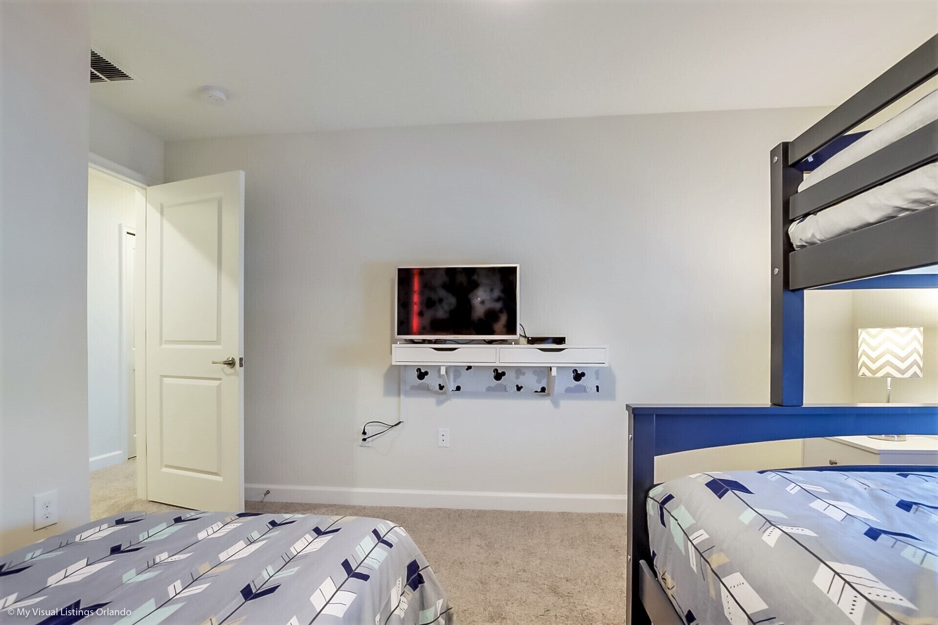 A bedroom with bunk beds, a TV on a shelf, and a desk with drawers.