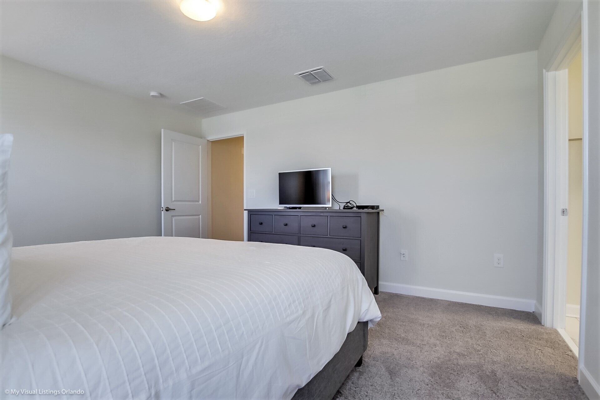 A bedroom with a bed, a dresser, a television, and a door.