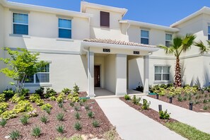 A modern apartment building with numbered units, a covered entrance, and a well-maintained garden with various plants and a palm tree.