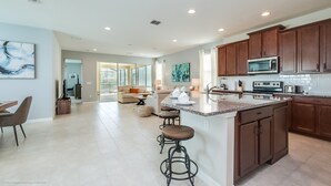A spacious kitchen with dark wooden cabinets, a large island with stools, and modern appliances. - 7 Bedroom 5 Bathroom with Spa & Game Room (Kissimmee)