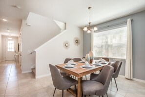 A dining area with a wooden table set for six, grey upholstered chairs, a chandelier, and a staircase leading to another room. - 7 Bedroom 5 Bathroom with Spa & Game Room (Kissimmee)